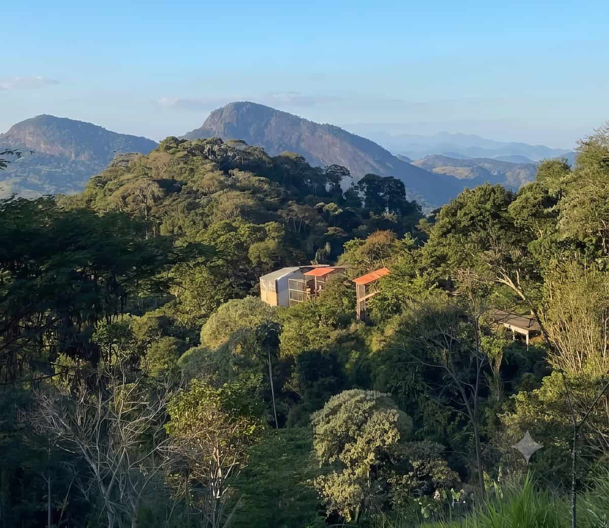 Construções da reserva em meio à mata, com serras ao fundo, em luz de fim de tarde