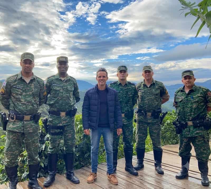 Wdson Ferreira Brum ao lado de cinco agentes da polícia ambiental, ao ar livre, com as serras e o céu da região ao fundo